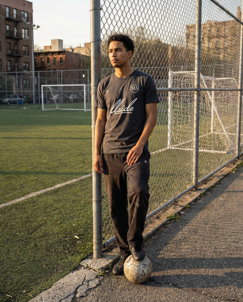 Person standing on a soccer field with a ball, wearing a dark t-shirt and pants.